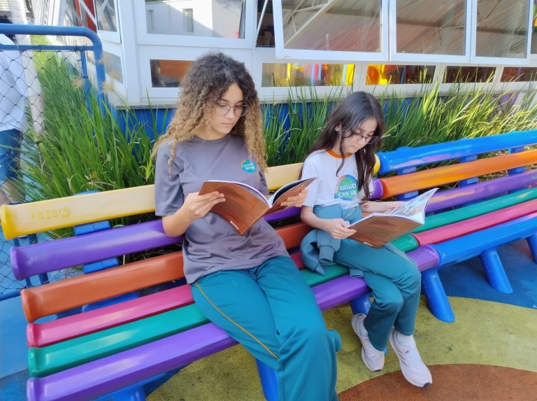 Alunas leem em um banco colorido do pátio