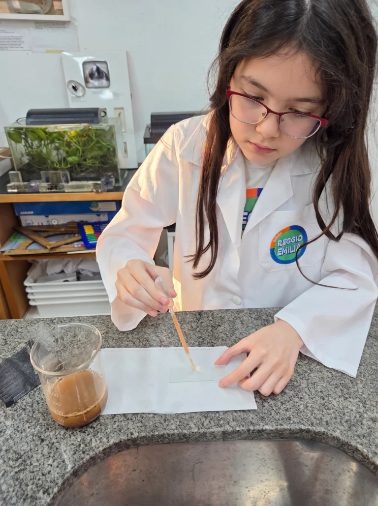 Aluna de jaleco faz uma experiência no laboratório